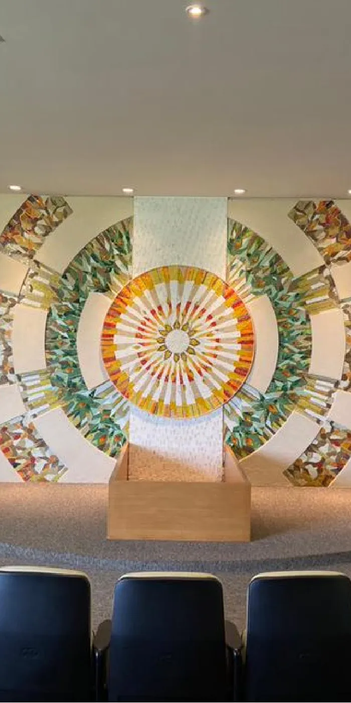 Interior de uma sala com cadeiras dispostas em arco, uma parede decorativa ao fundo e telas de apresentação.