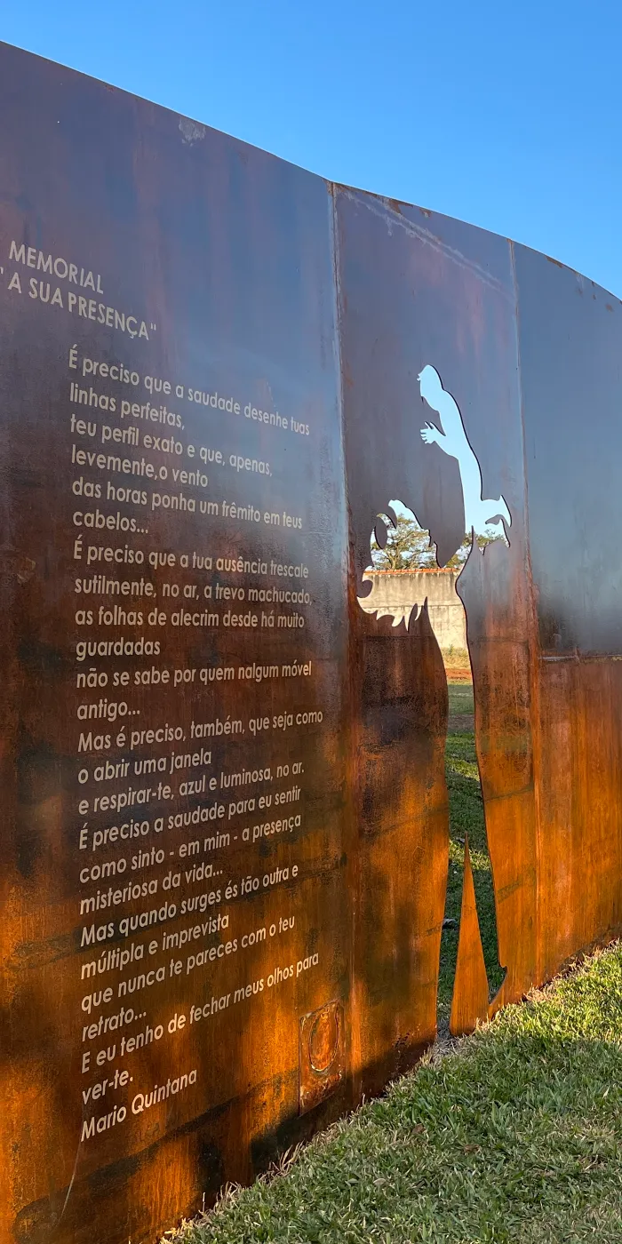 Instalação artística ao ar livre com painéis de metal cortado, apresentando figuras e textos, em um espaço verde.